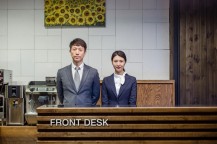 FRONT　DESKと書かれた台の後ろに男性1人と女性1人が立っている。