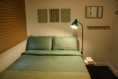 グリーンのベッドに照明が当てられている。枕もとの壁にはグリーン系統の柄で飾られている。