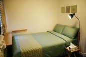 やさしいグリーンのベッドがあり、枕もとに照明がある。